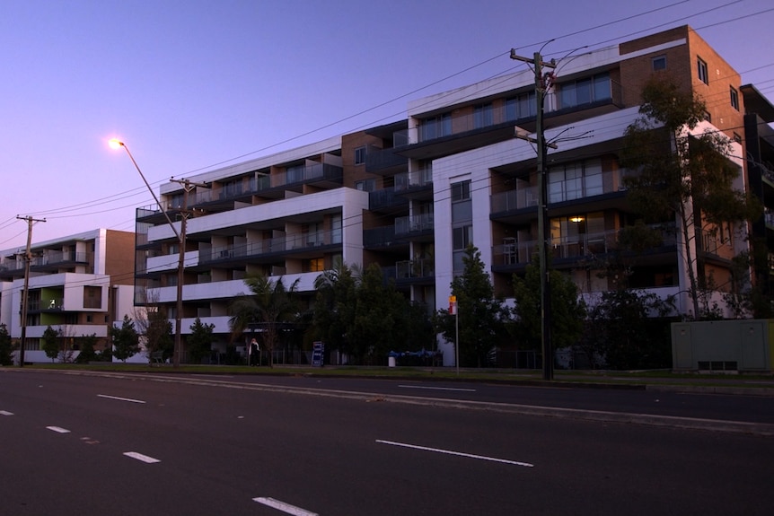 A modern six-level apartment building on a road.