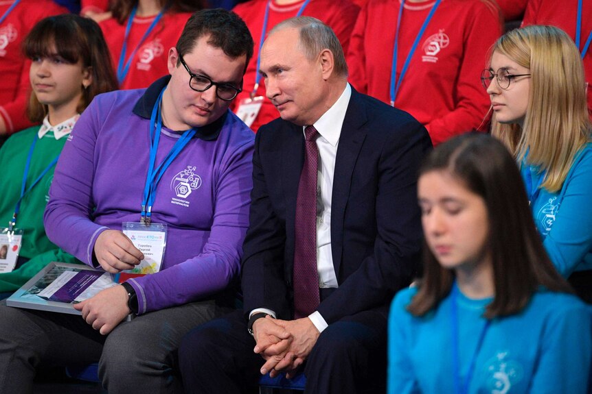 A young man whispers into Russian President Vladimir Putin's ear during a youth forum.