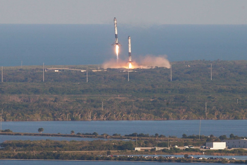 With flames underneath them, two rocket boosters approach landing pads.