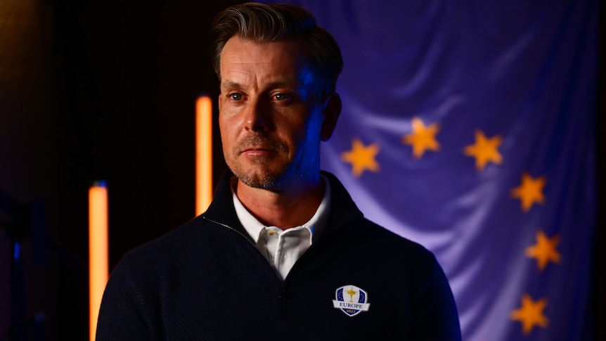 A man wearing a Team Europe jacket stands for a photo session with a European flag in the background.