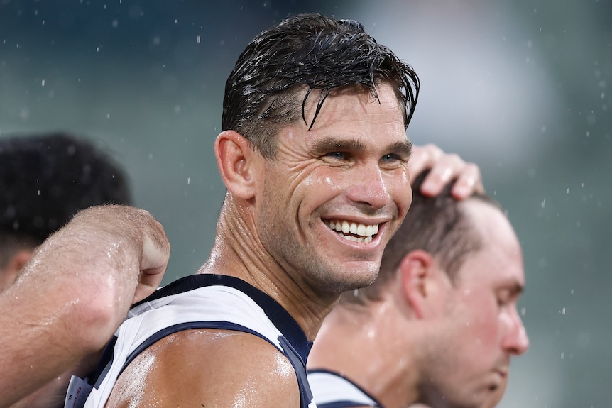 Tom Hawkins dari Geelong Cats tersenyum di tengah hujan selama pertandingan AFL.