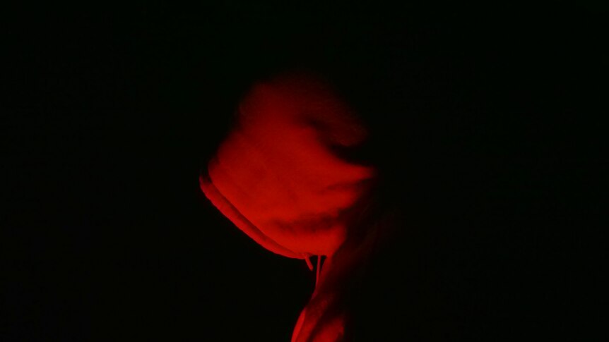 Hooded person at night looking down.