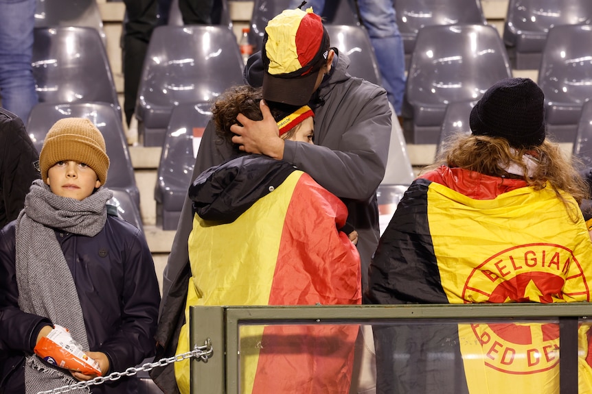 Soccer fans in Belgian flags in the stands of a stadium. A man and woman hugging tightly