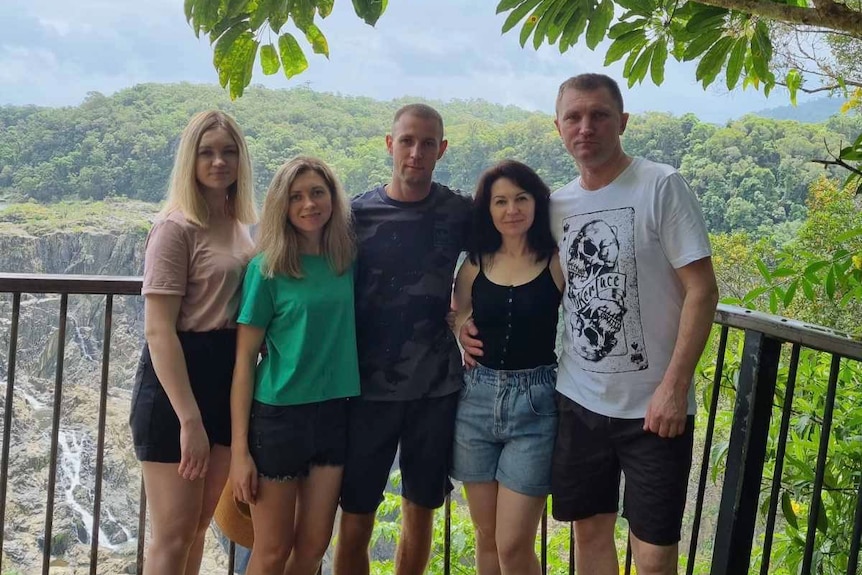 family of five posing for a photo at a lookout with rain-forest  behind