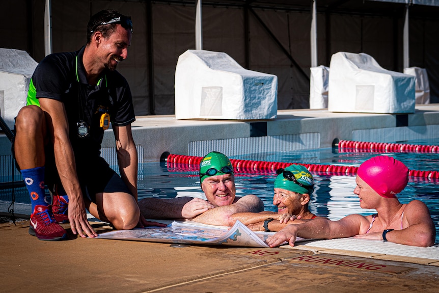 Three swimmers in a pool with a coach hunkering. All looking at a navigation chart.