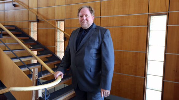 Professor Newsholme standing near a staircase and holding the rail.