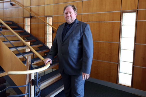 Professor Newsholme standing near a staircase and holding the rail.