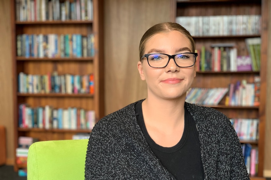 A young woman in glasses with bookshelves in the background