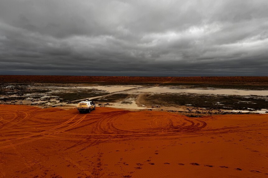 vehicle on red sand dune looking over muddy claypan
