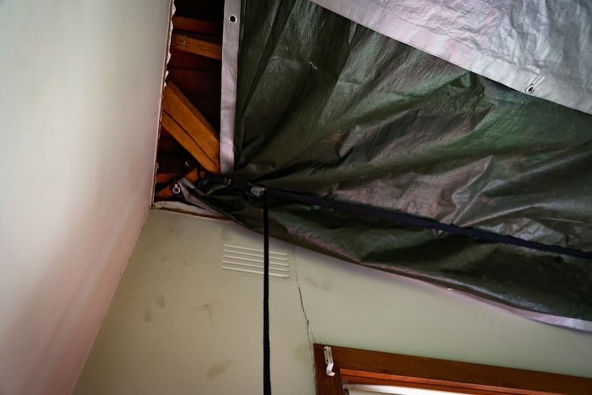 Exposed wooden beams in an open ceiling with a makeshift tarp covering the gaping hole.