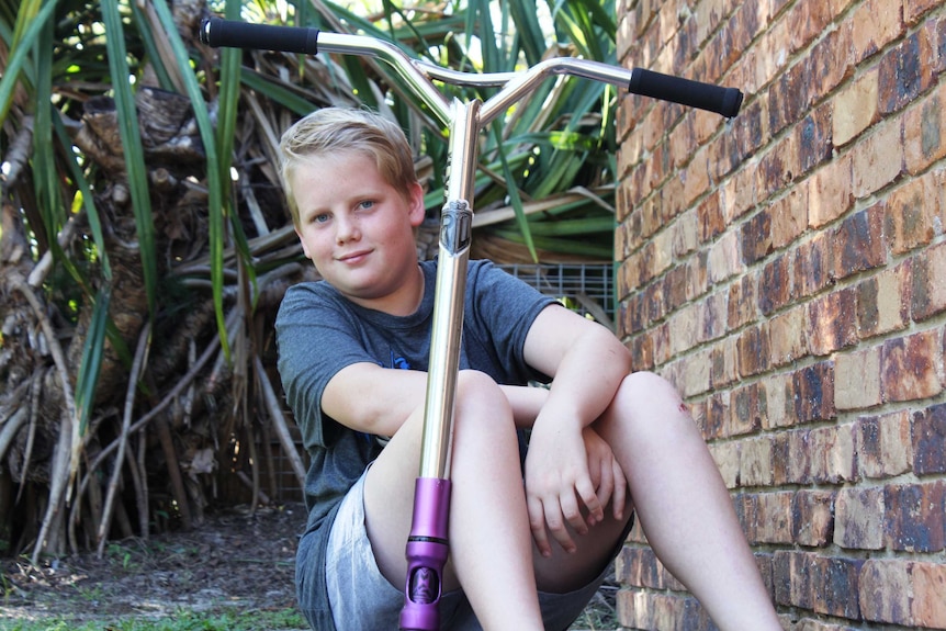 13yo Oliver, who has Tourette syndrome, sits smiling on his scooter