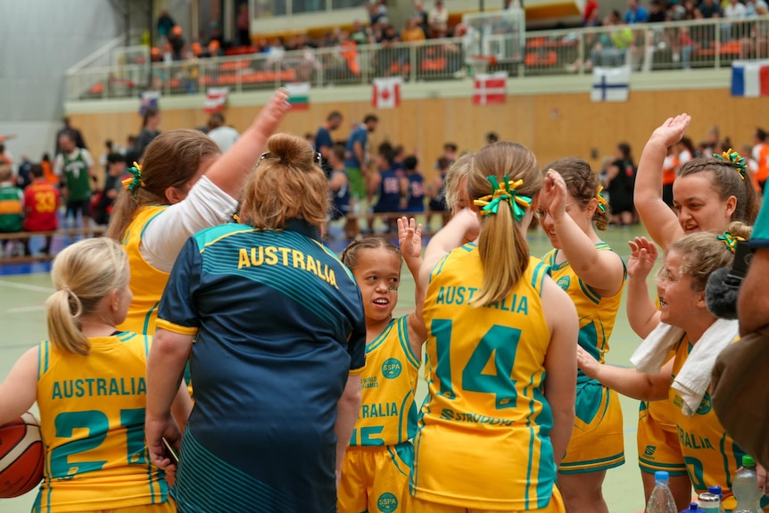 A group of short statured female basketballers stand together in a loose huddle, smiling. 
