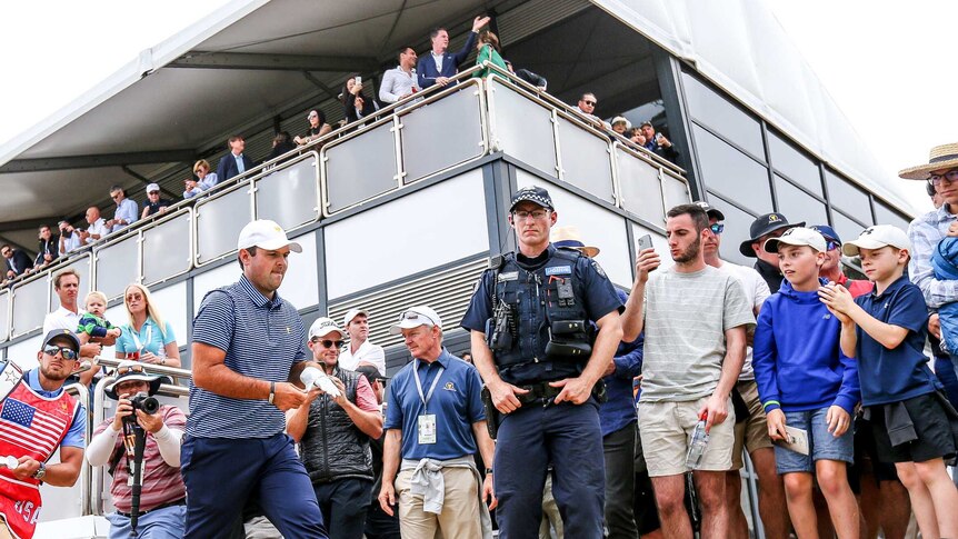US golfer Patrick Reed walks on the course as spectators and police watch on.