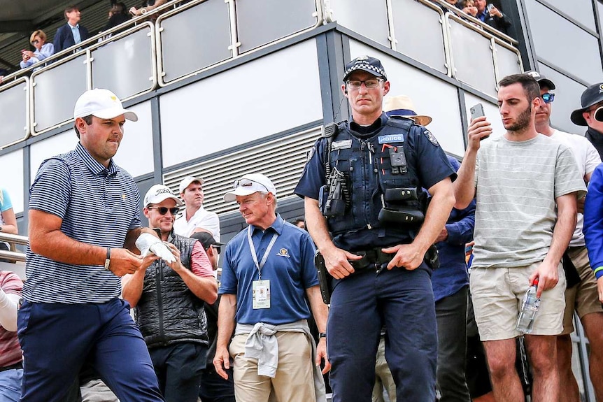 US golfer Patrick Reed walks on the course as spectators and police watch on.