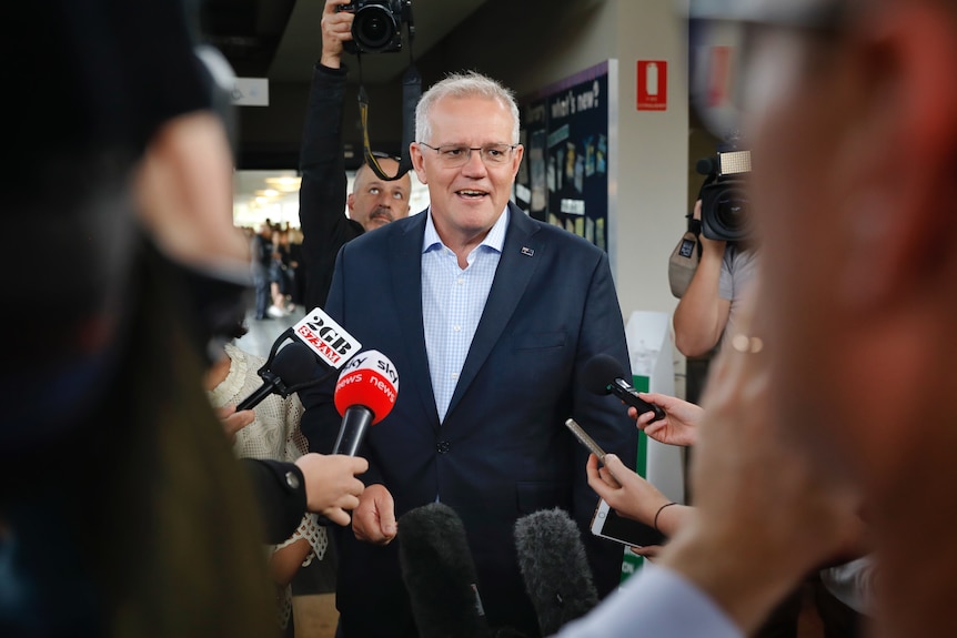 Scott Morrison, wearing a suit, stands and answers questions from journalists holding microphones.