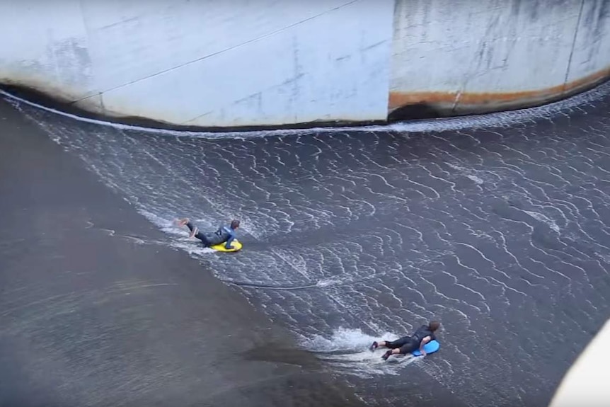 Two people surfing down a dam.