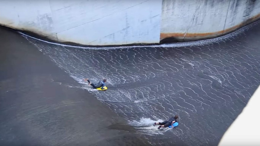 Two people surfing down a dam.