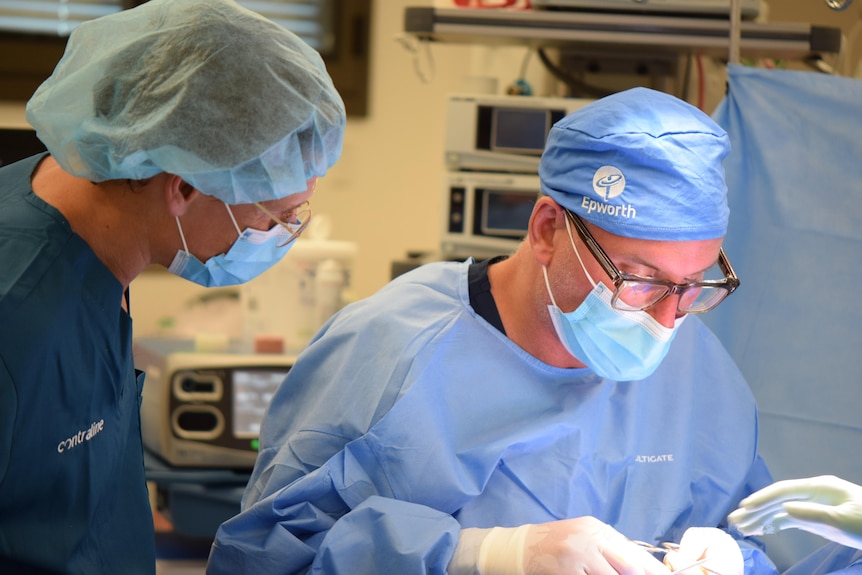 Two men wearing surgical scrubs are in an operating theatre performing a procedure