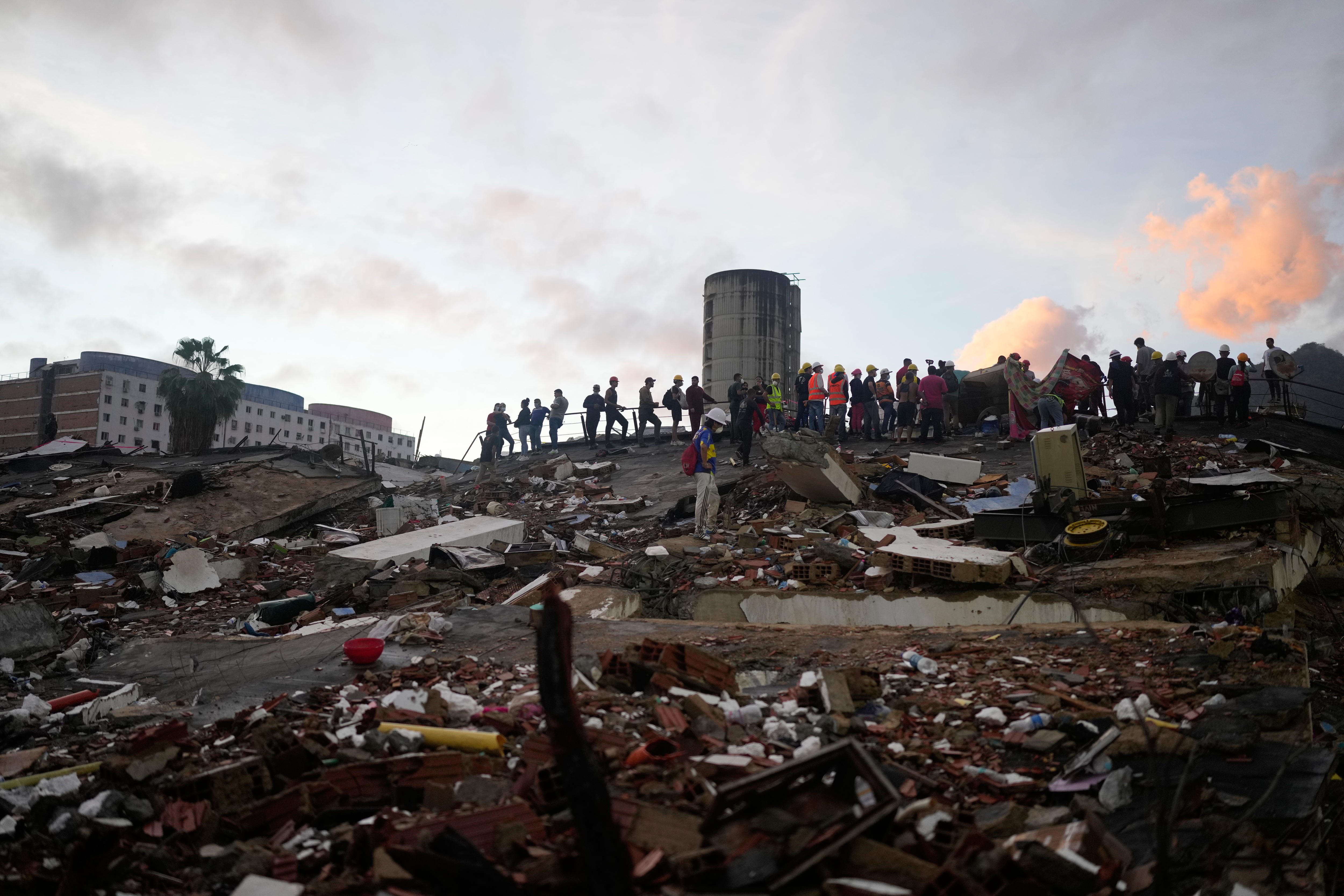 Silhouettes of a line of rescuers in hi-vis clothing and helmets standing on the horizon of a mountain of rubble.