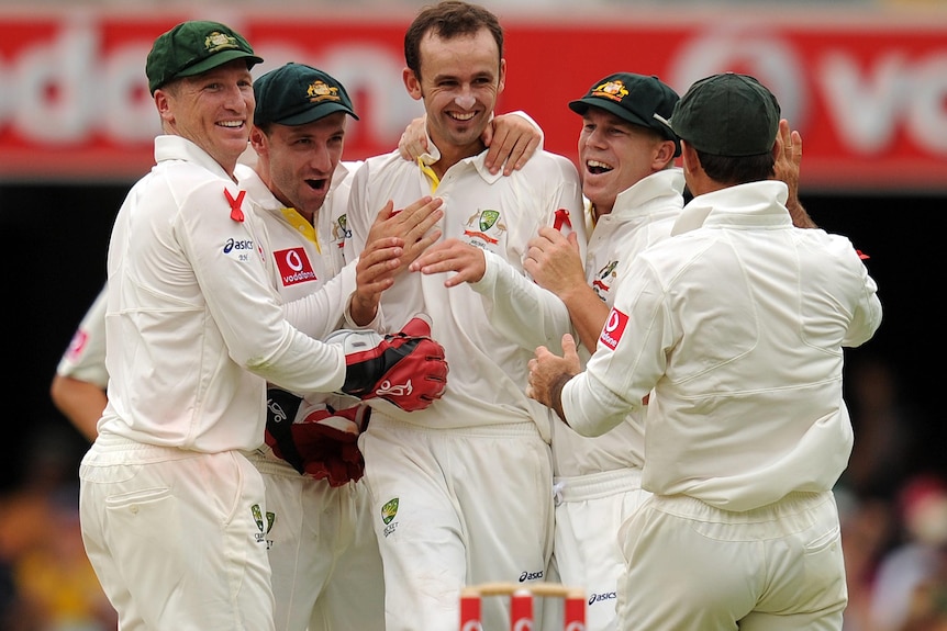 Nathan Lyon is hugged by team-mates after taking his first Test wicket.