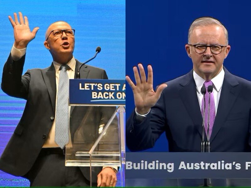 Two men in suits hold up their right hands in a wave