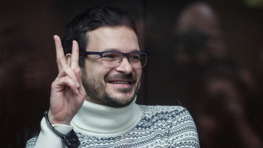 Ilya Yashin gestures with two fingers in peace sign while handcuffed inside a glass cage in a Moscow court.