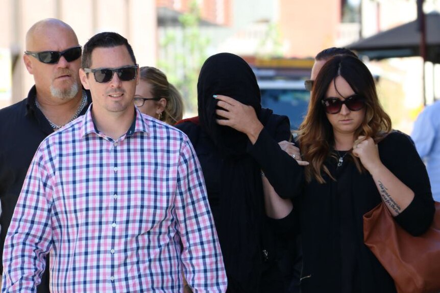 Janet Kirby, with a black scarf covering her face, walks down a Perth street flanked by a group of supporters.