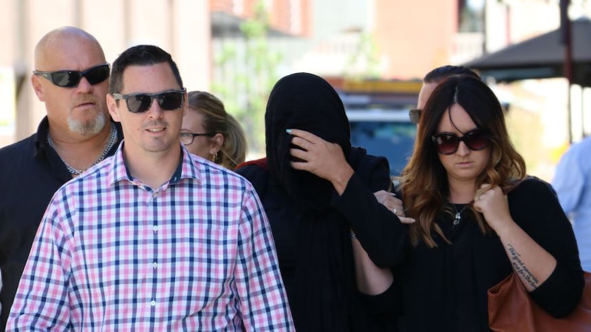 Janet Kirby, with a black scarf covering her face, walks down a Perth street flanked by a group of supporters.