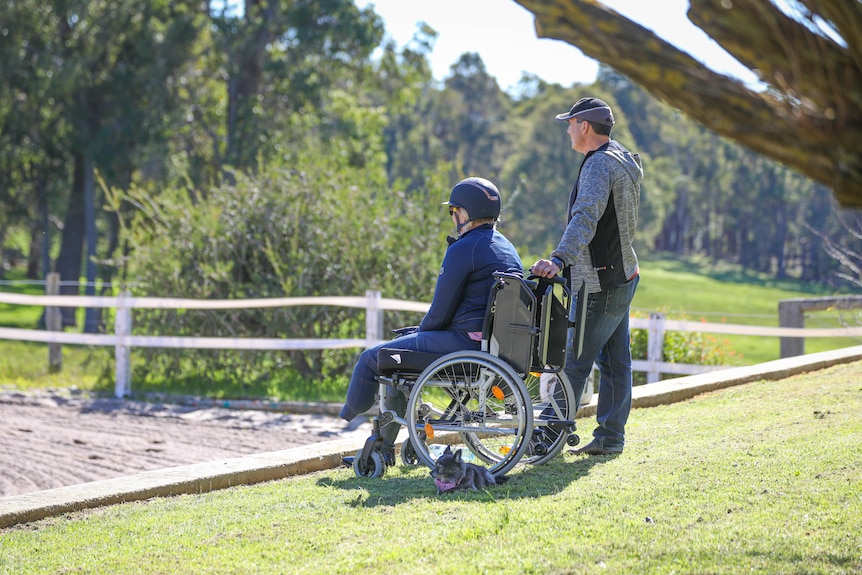 A woman in a wheelchair looks off into the distance, next to her husband.