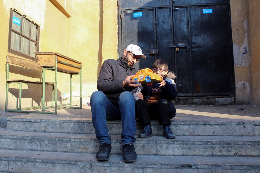A man and a boy sit on a set of stairs and the boy plays with a toy.