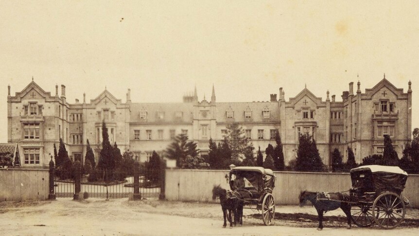 A sepia photo shows a gothic mansion-like building, with a black wrought-iron gate and horse carriages parked in front.