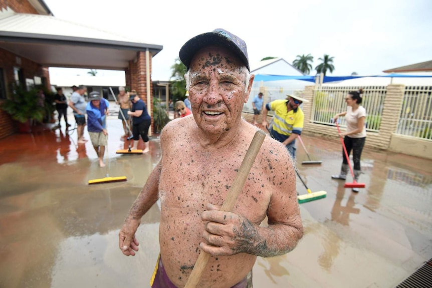 Dave Mitchell, covered in mud, holds a broom as he helps clean his brother's flood-affected motel in Townsville.