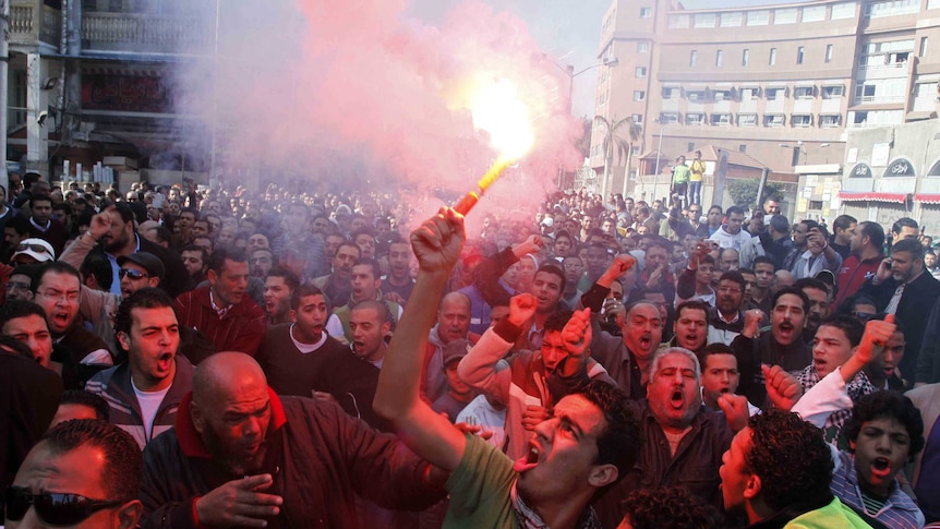 An Egyptian protester and fan of al-Masry football club waves a flare as others chant slogans during a demonstration.