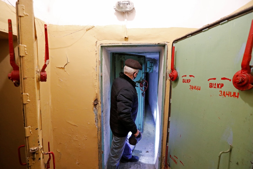 A man stands at a door with a flashlight pointed down a tunnel.