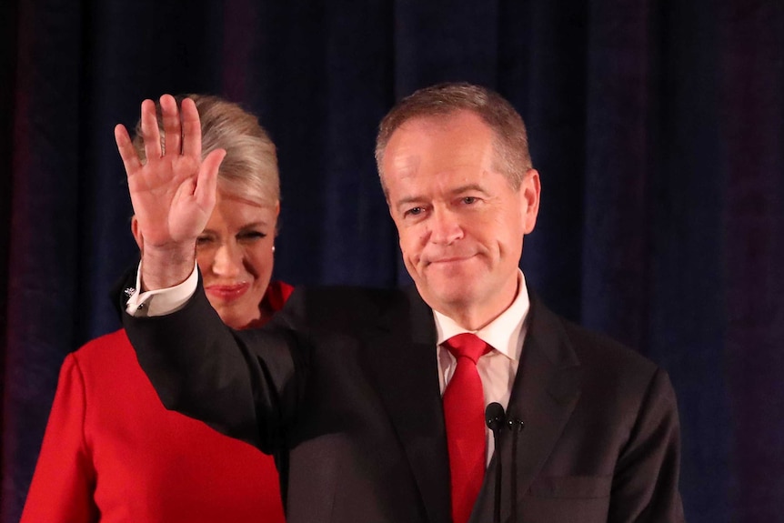 Chloe Shorten, dressed in red, stands next to Bill Shorten as he waves.