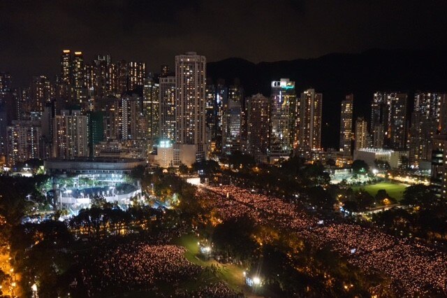 A bird's eye view of the skyscrapers lit up at night and the crowds below.
