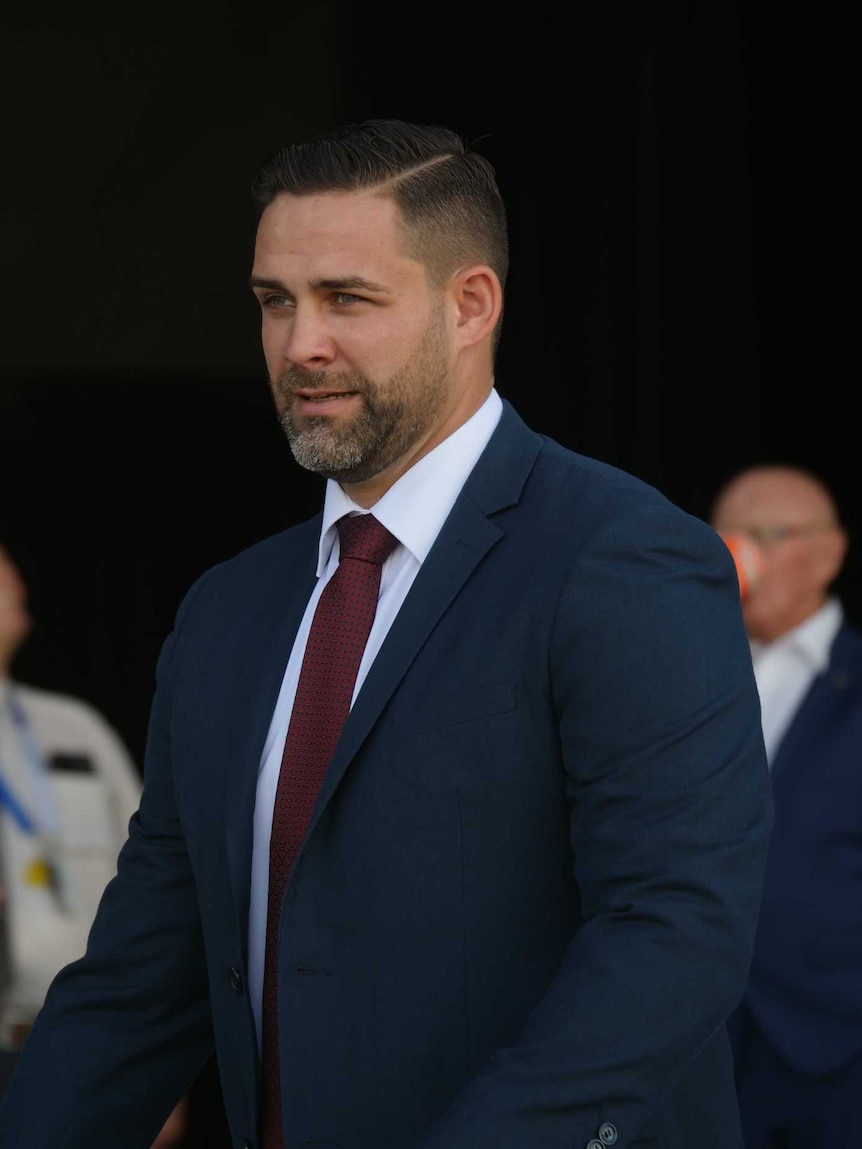 A dark-haired, bearded man wearing a dark suit.