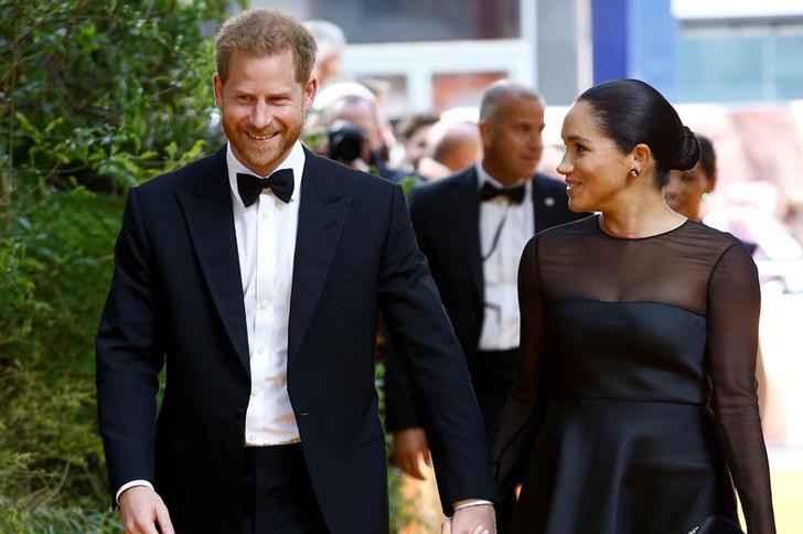 Prince Harry laughs and looks down as he walks next to Meghan holding her hand. She looks to him, and they are both in black tie
