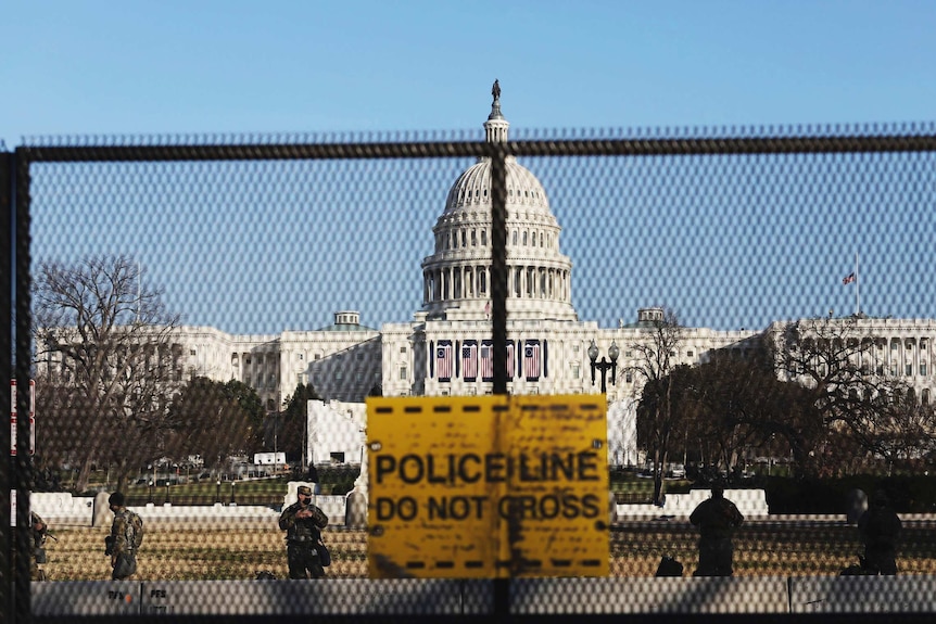 A security fence displays a sign saying Police Lines do not cross as guards walk around behind it.