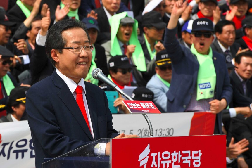 South Korean presidential candidate Hong Jun-Pyo stands at a lectern, at a rally, with enthusiastic supporters in the background