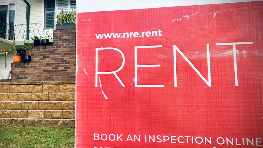 A red sign with white writing that says 'rent' in capital letters that obscures a weatherboard house in the background.