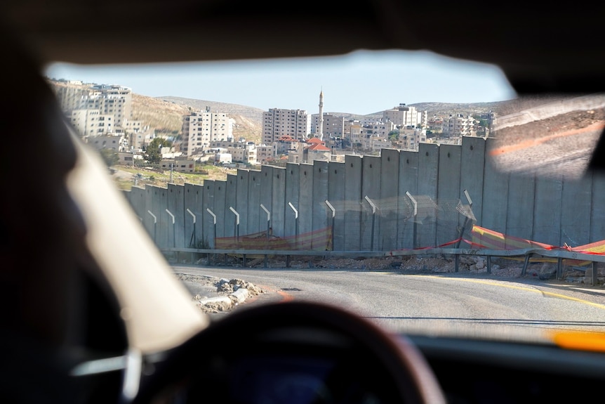 A large concrete wall lines the side of a road. The photo has been taken from inside a car.