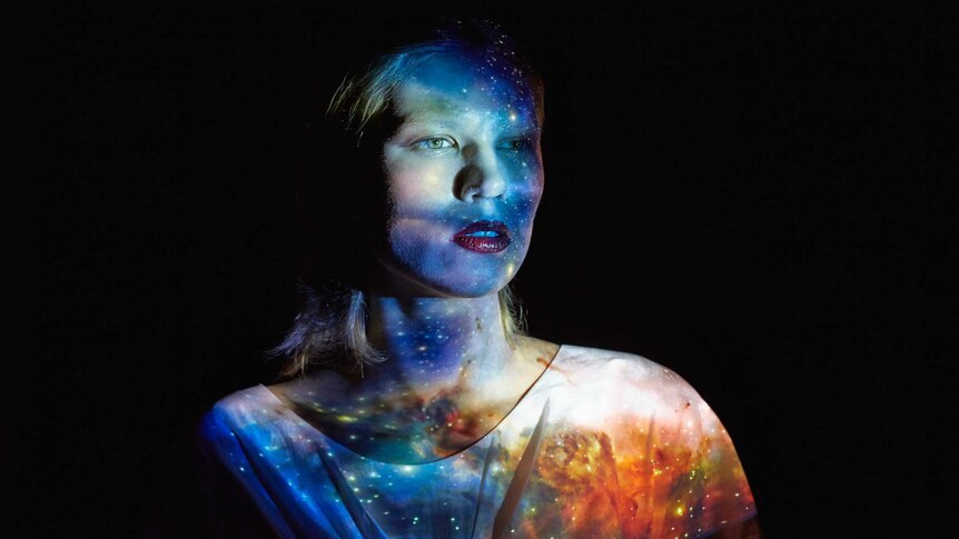 young caucasian woman wearing white shirt with milky way universe pattern reflected onto her, against black background