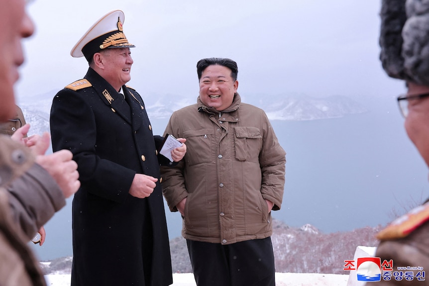 North Korean leader Kim Jong Un smiles in the snow with hands in pockets next to military leaders