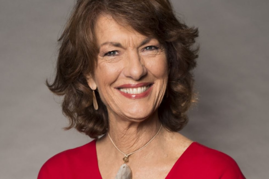 Geraldine Doogue, with wavy brown hair and wide smile, wears a red top with a small silver necklace.