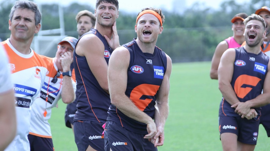 Heath Shaw and GWS Giants teammates in uniform stand together on the field, all looking skyward.