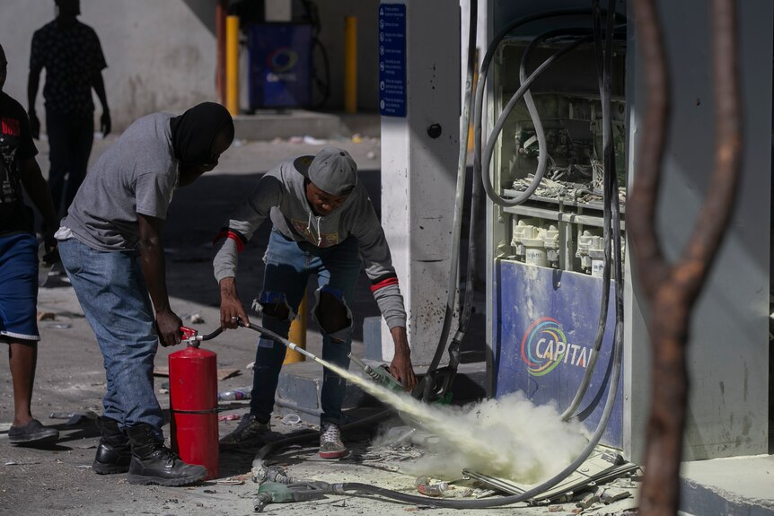 Two security guards extinguish a fire near a petrol pump with a fire extinguisher