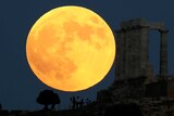 People watch a full moon rising behind the Temple of Poseidon.