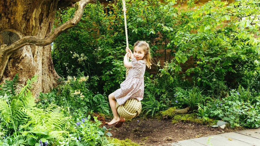 Princess Charlotte looks over her shoulder while sitting on a rope swing, surrounded by foliage