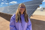 A woman in a purple jumper standing in front of a solar panel. 